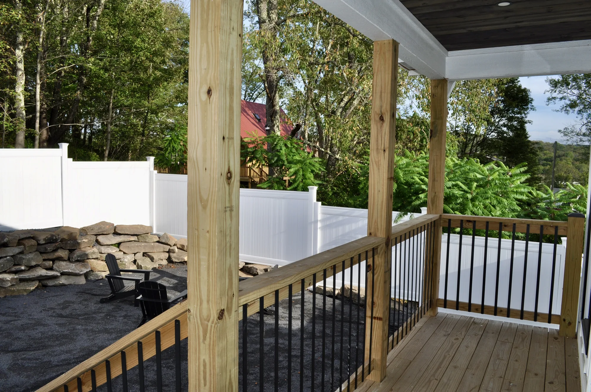 Covered deck with Adirondack chairs overlooking the fenced yard and stone wall